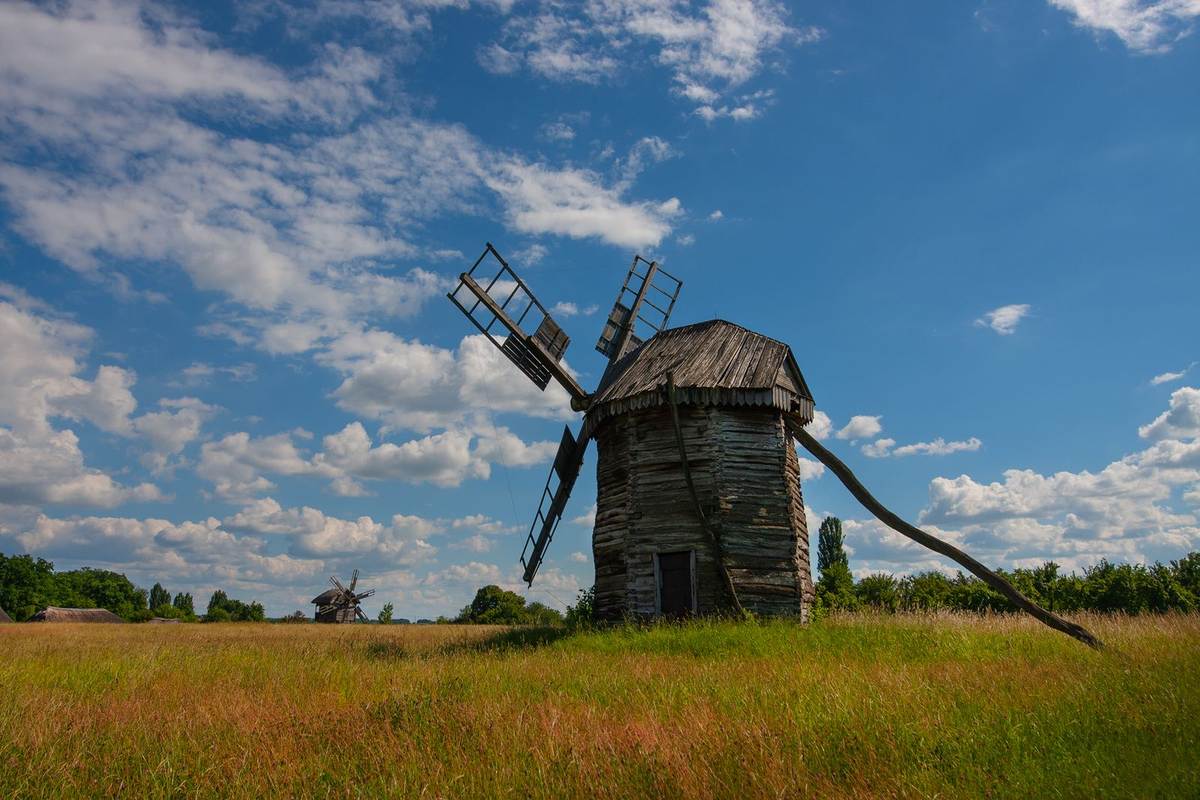 Alte Holzwindmühle auf einer sonnigen Wiese unter blauem Himmel