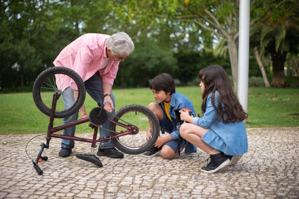 Älterer Mann repariert im sonnigen Park mit zwei Kindern ein Fahrrad