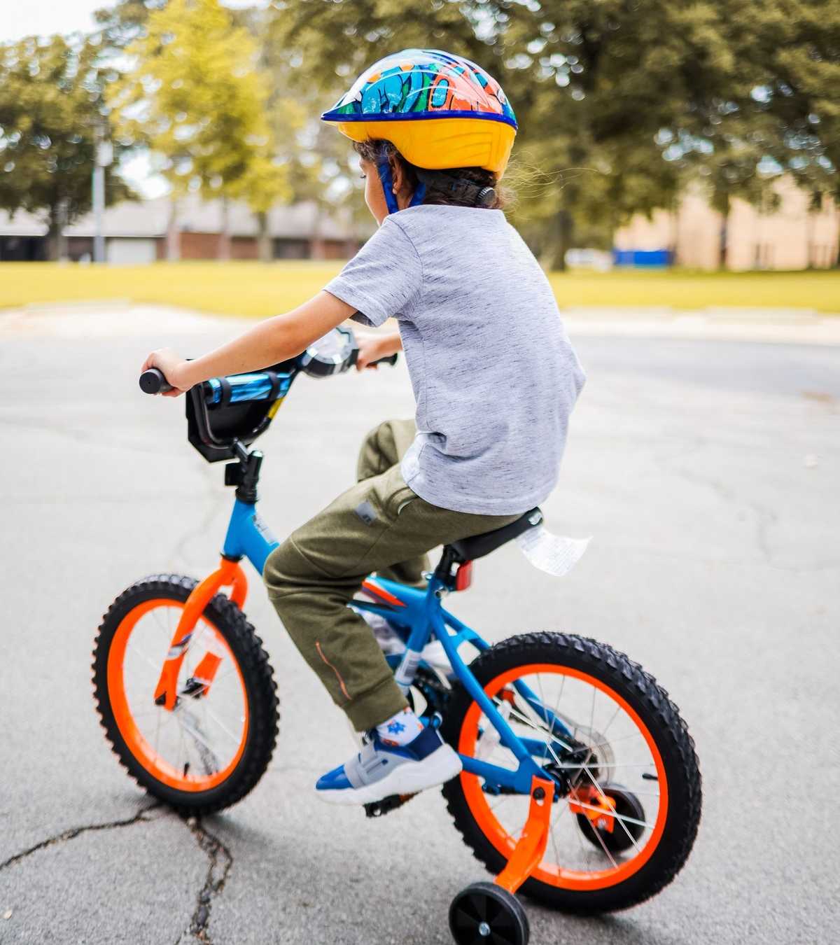 Kind mit buntem Helm fährt fröhlich Fahrrad mit Stützrädern