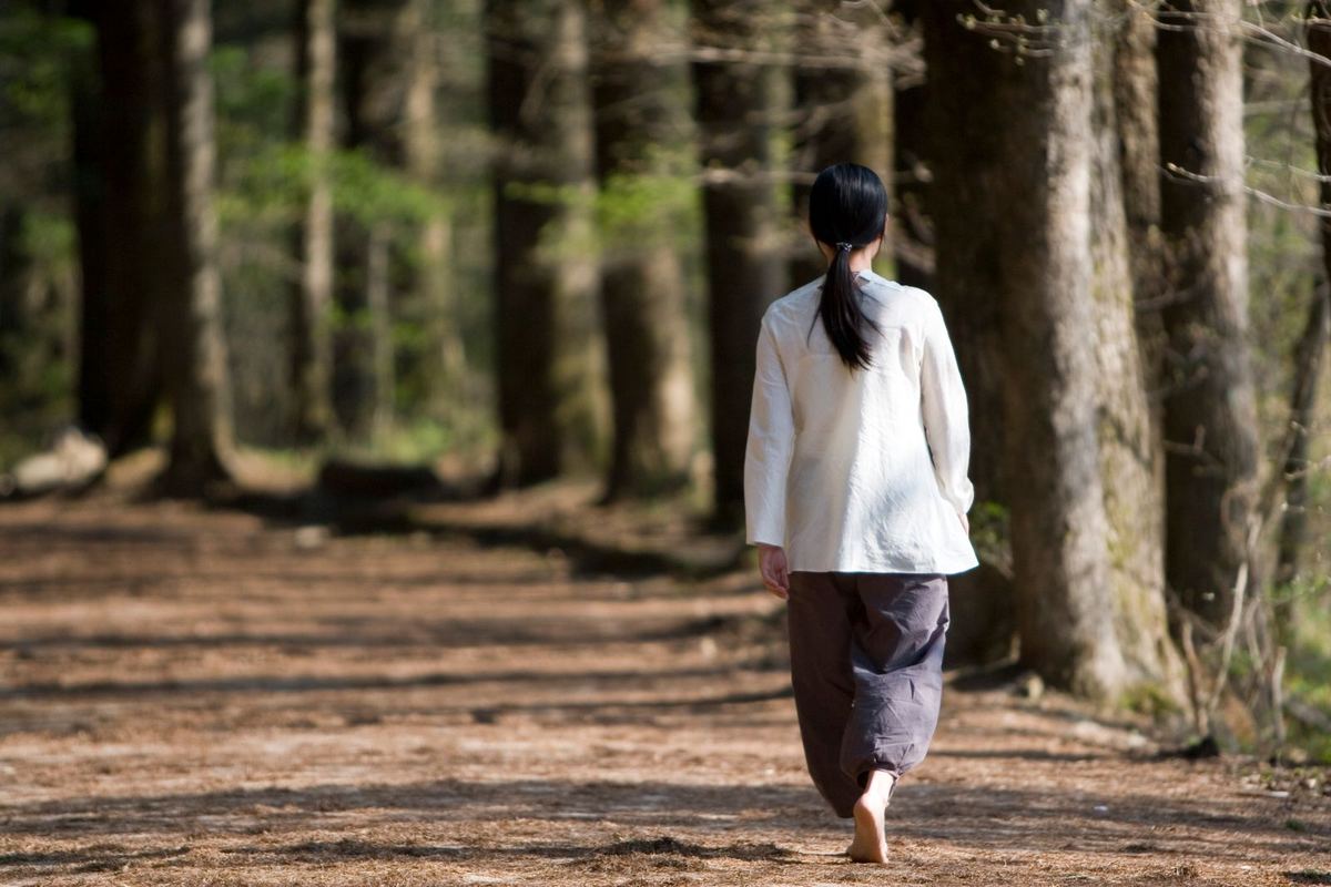 Frau geht barfuß auf einem sonnigen Waldweg
