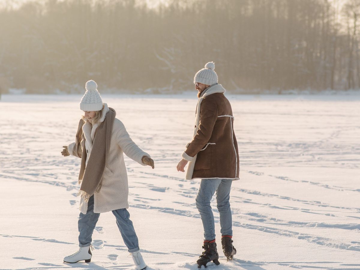 Zwei Menschen in Wintermänteln laufen Schlittschuh auf einem verschneiten, zugefrorenen See im Abendlicht